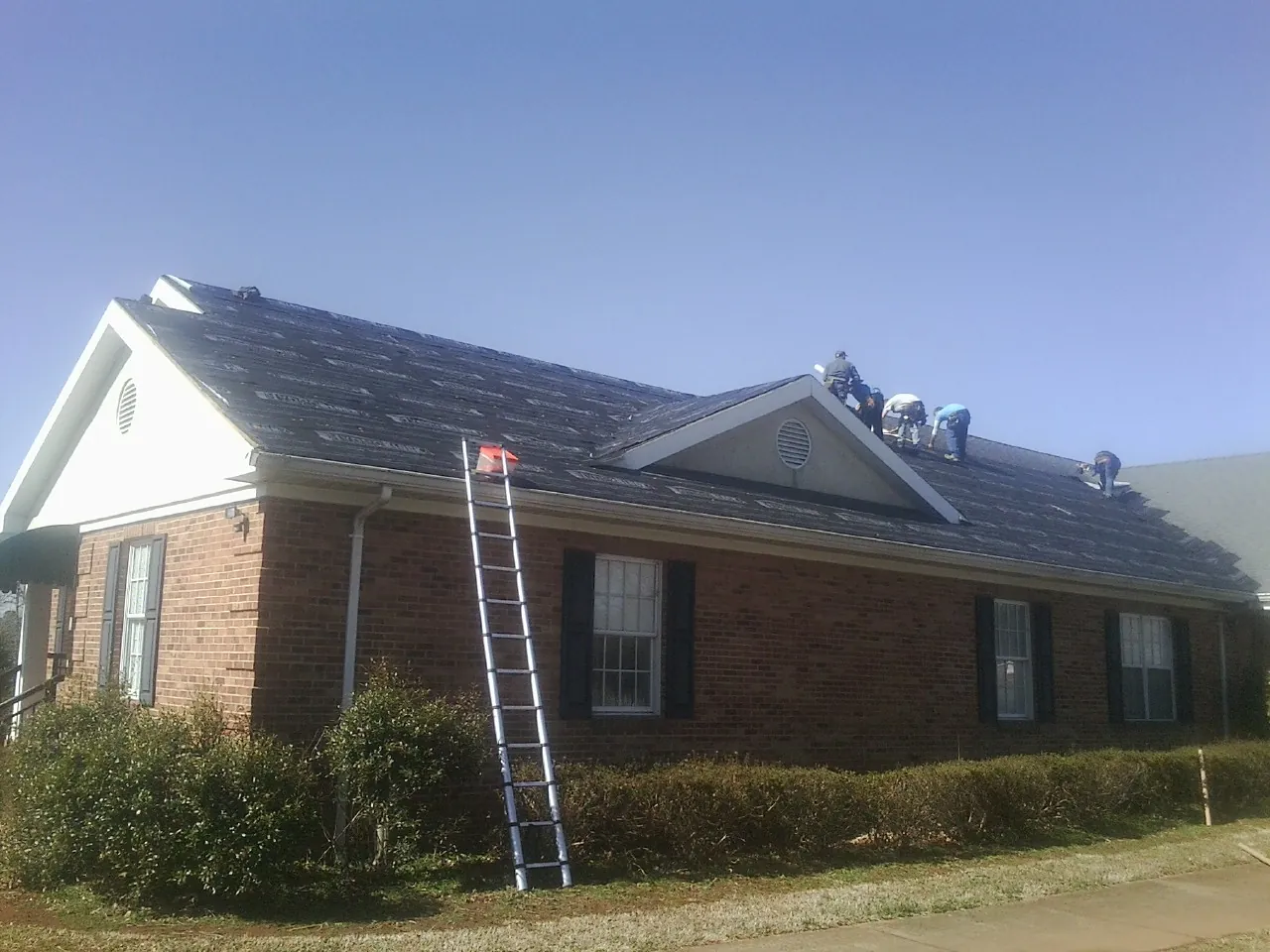Crew tearing shingles off a brick ranch roof with a ladder set — Emergency Roof Repair work by our crew in Apalachin