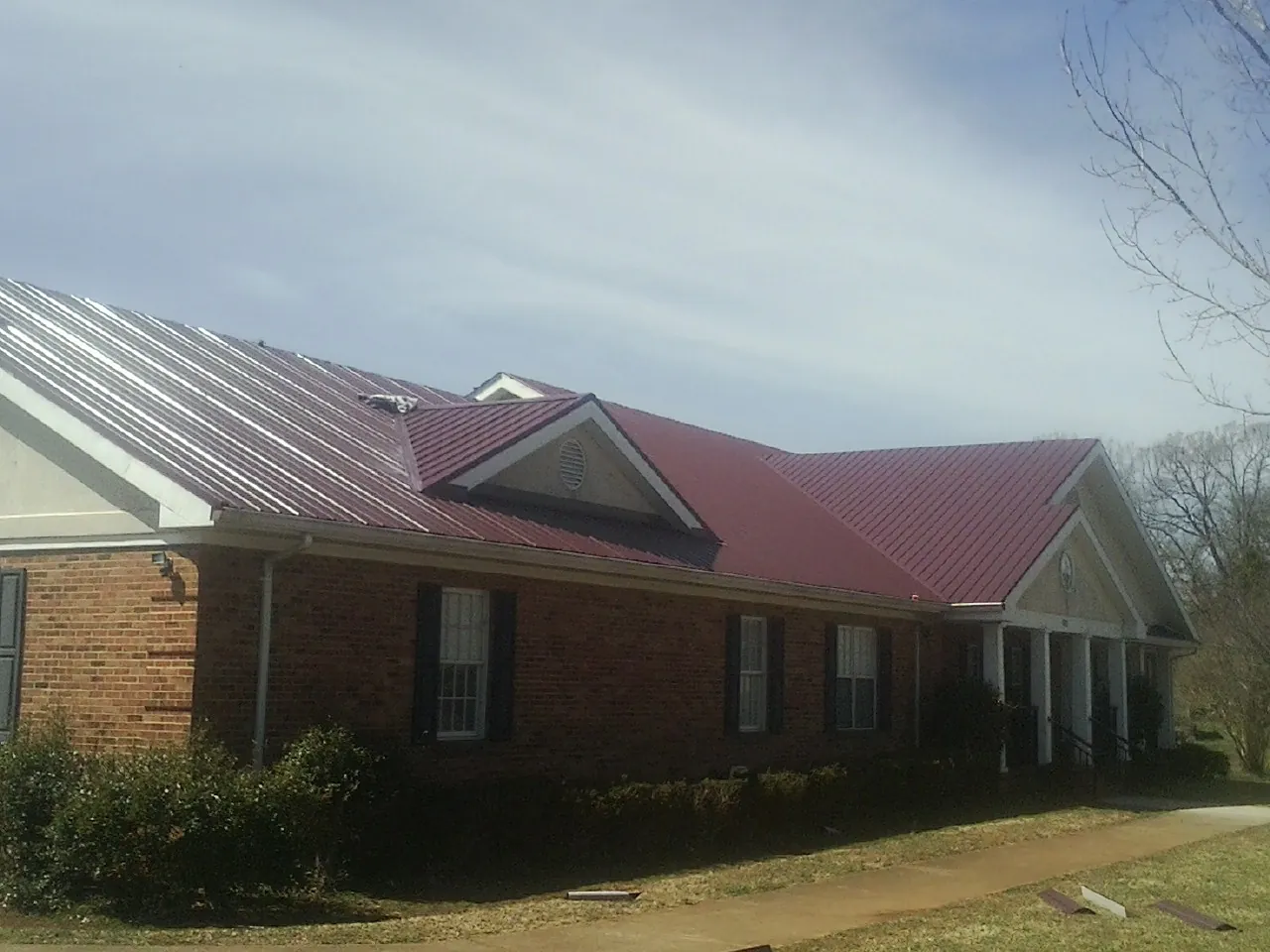Red metal roof with gabled entries on a long brick building, from a Hail Damage Roof Repair job in Apalachin