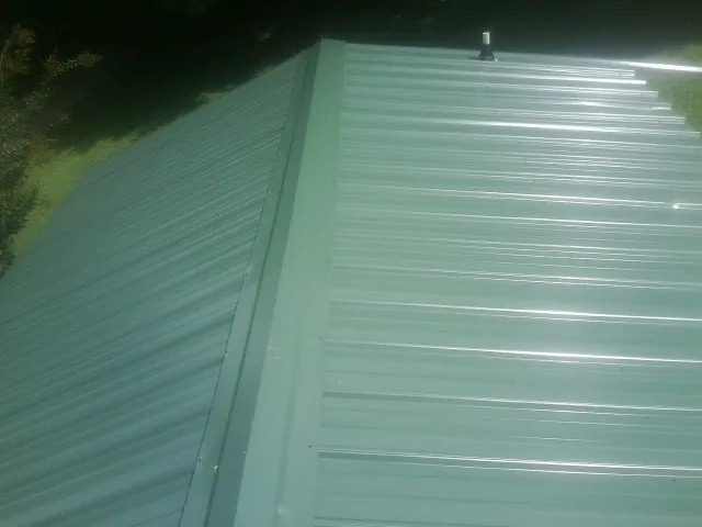 New green metal panels meeting at the ridge of a roof — Flat Roof Repair work by our crew in Apalachin