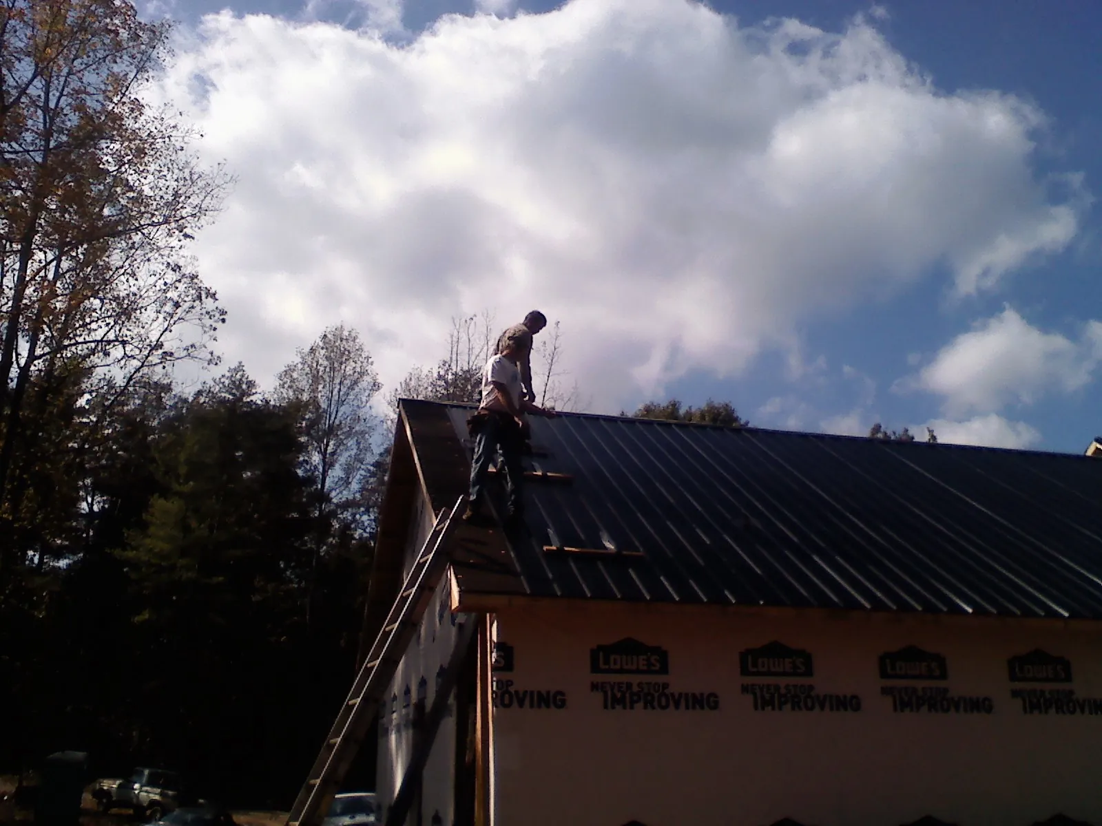 Roofer fastening dark metal panels high against a cloudy sky, from a Roof Inspection job in Apalachin