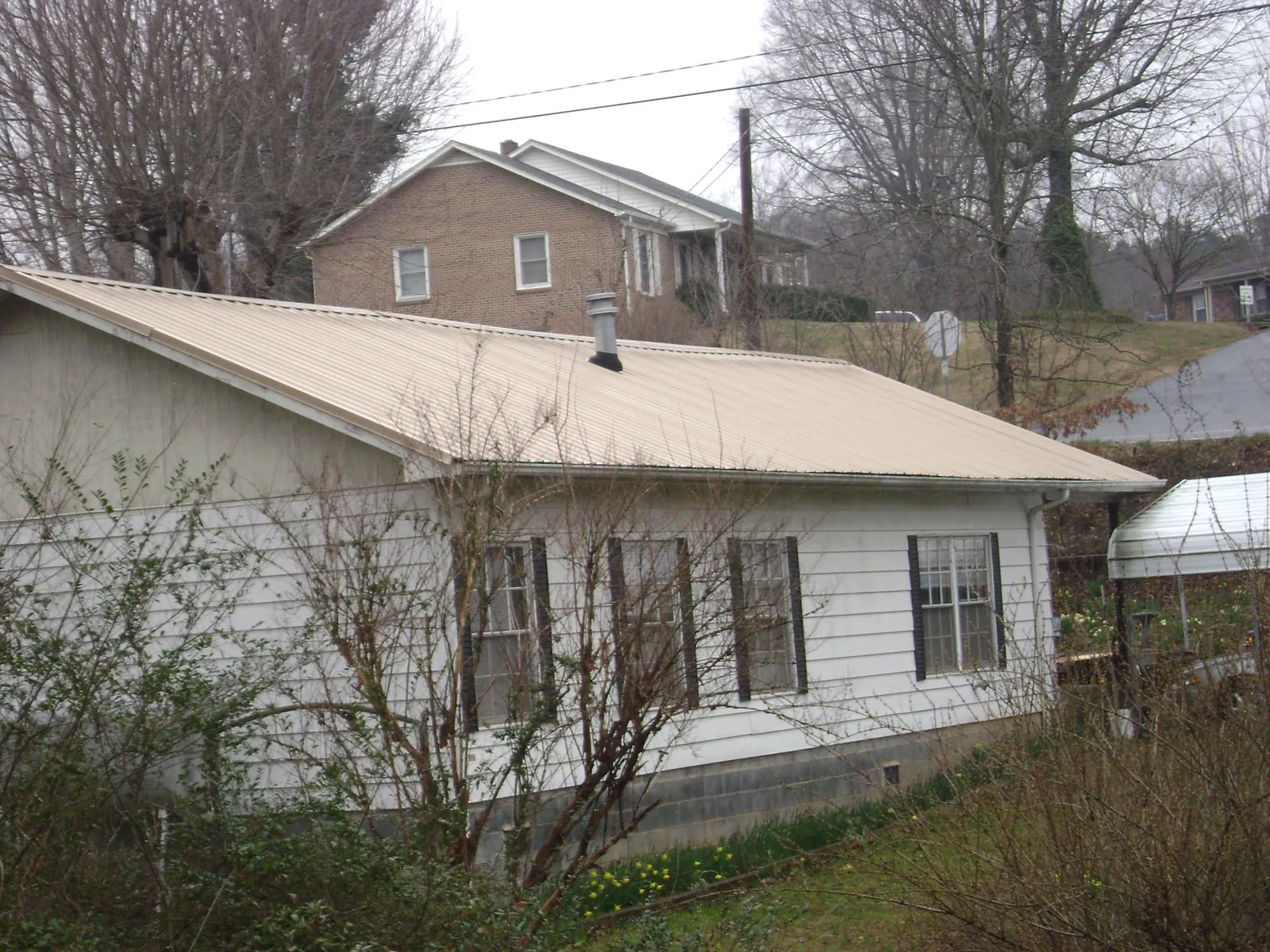 Tan metal roof on a white sided house set into a hillside — Commercial Roofing by Roofing Brothers in Apalachin
